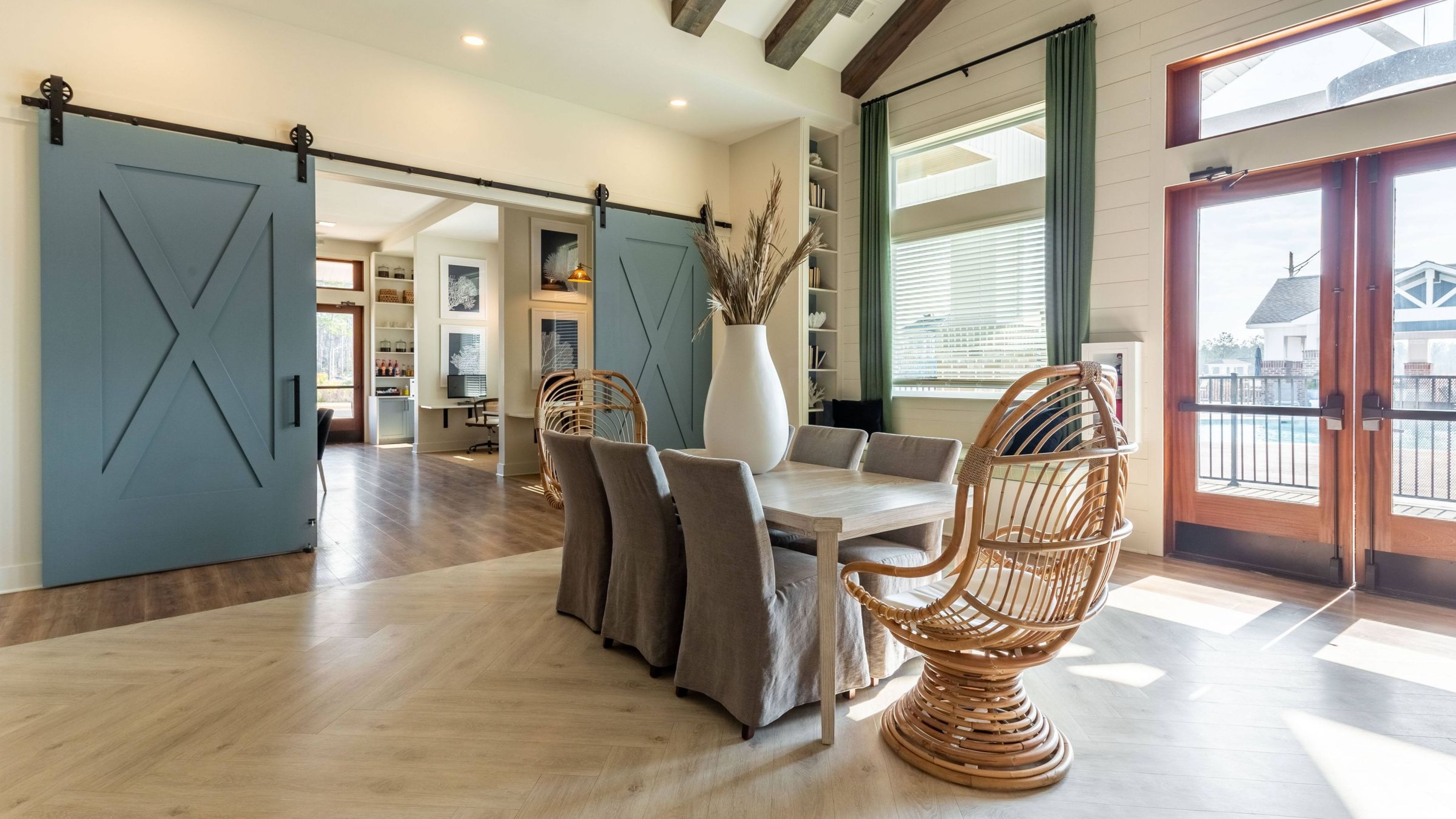 Hawthorne Waterside airy dining area with rustic beams, sliding barn doors, and a unique rattan egg chair near the exit.
