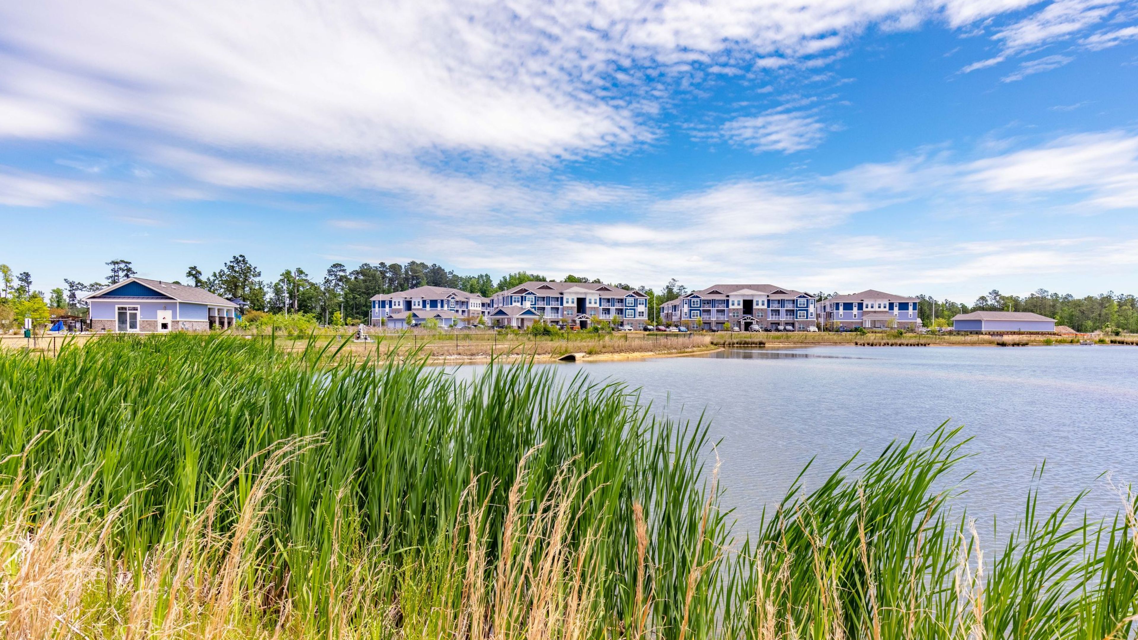 Hawthorne Waterside serene lakeside setting with lush greenery and a view of contemporary apartment buildings in the distance.